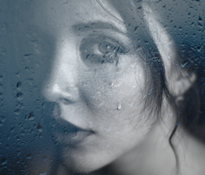 Woman crying behind glass sprinkled with rain water
